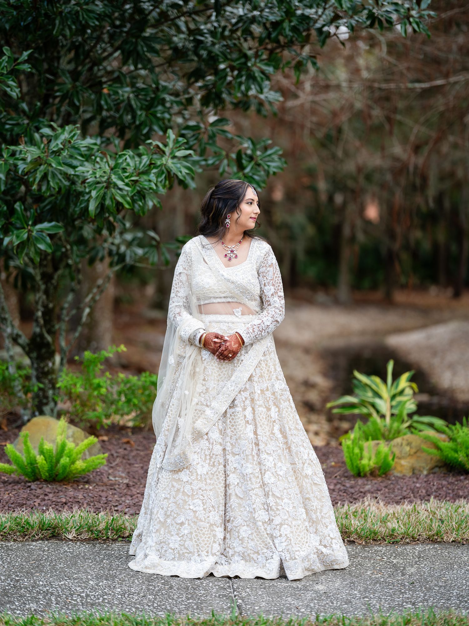 Elegant white lace wedding gown photographed in a natural garden setting.