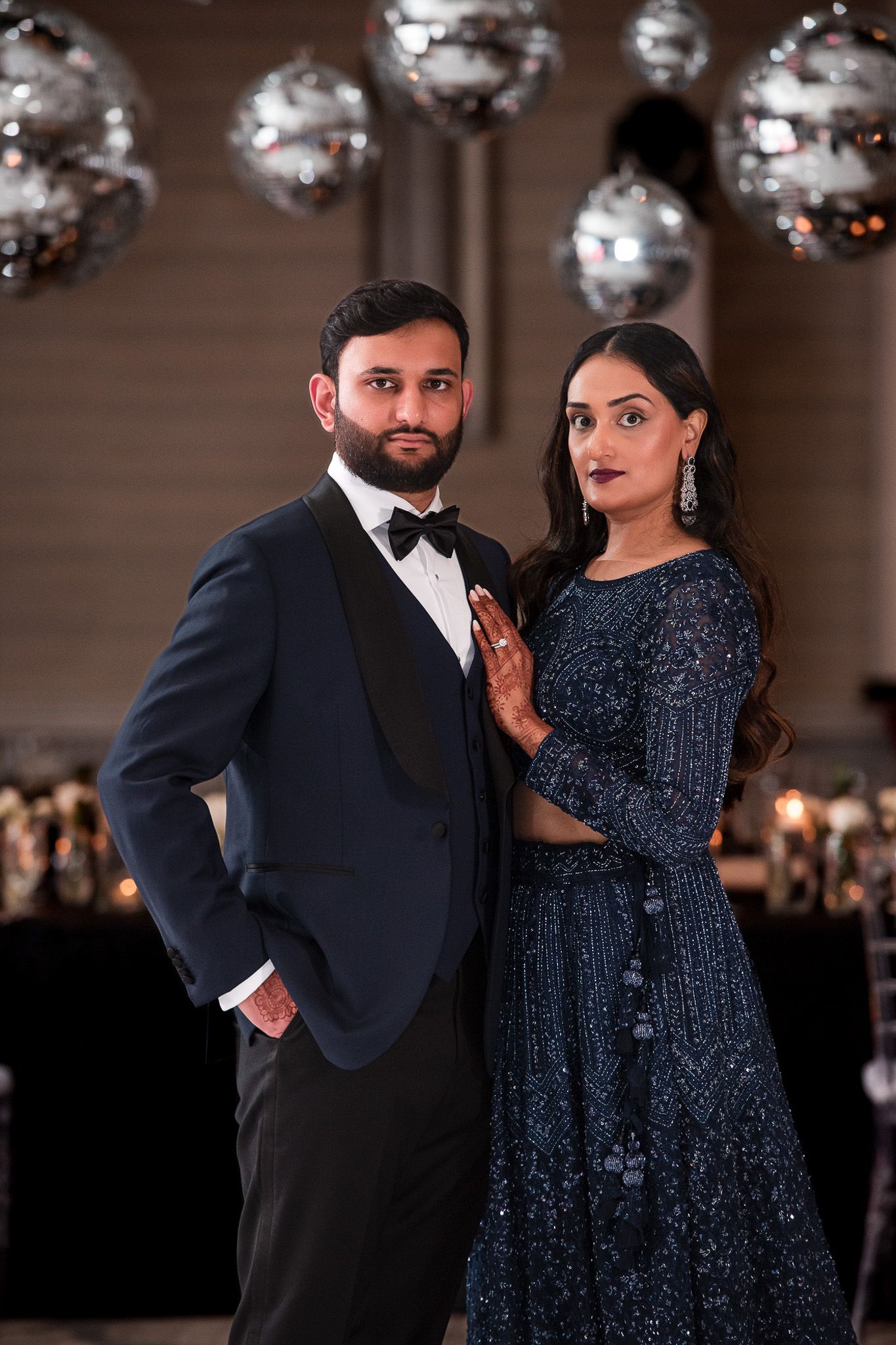 Formal portrait of couple in evening attire beneath sparkling disco balls at an elegant reception.