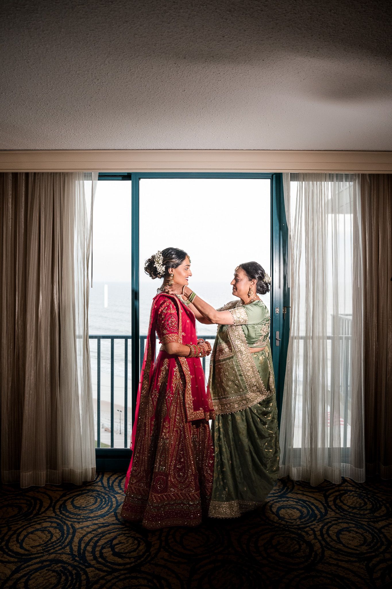 Two figures in elegant traditional attire sharing intimate moment by window with city view.
