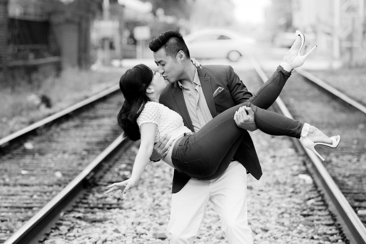 Black and white romantic photo of couple posing playfully on train tracks.