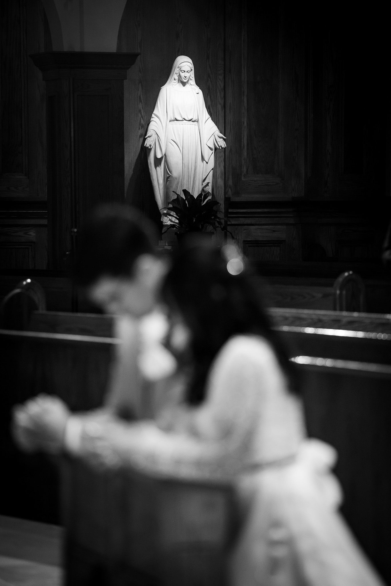 Religious statue in a church with blurred wedding ceremony in foreground.