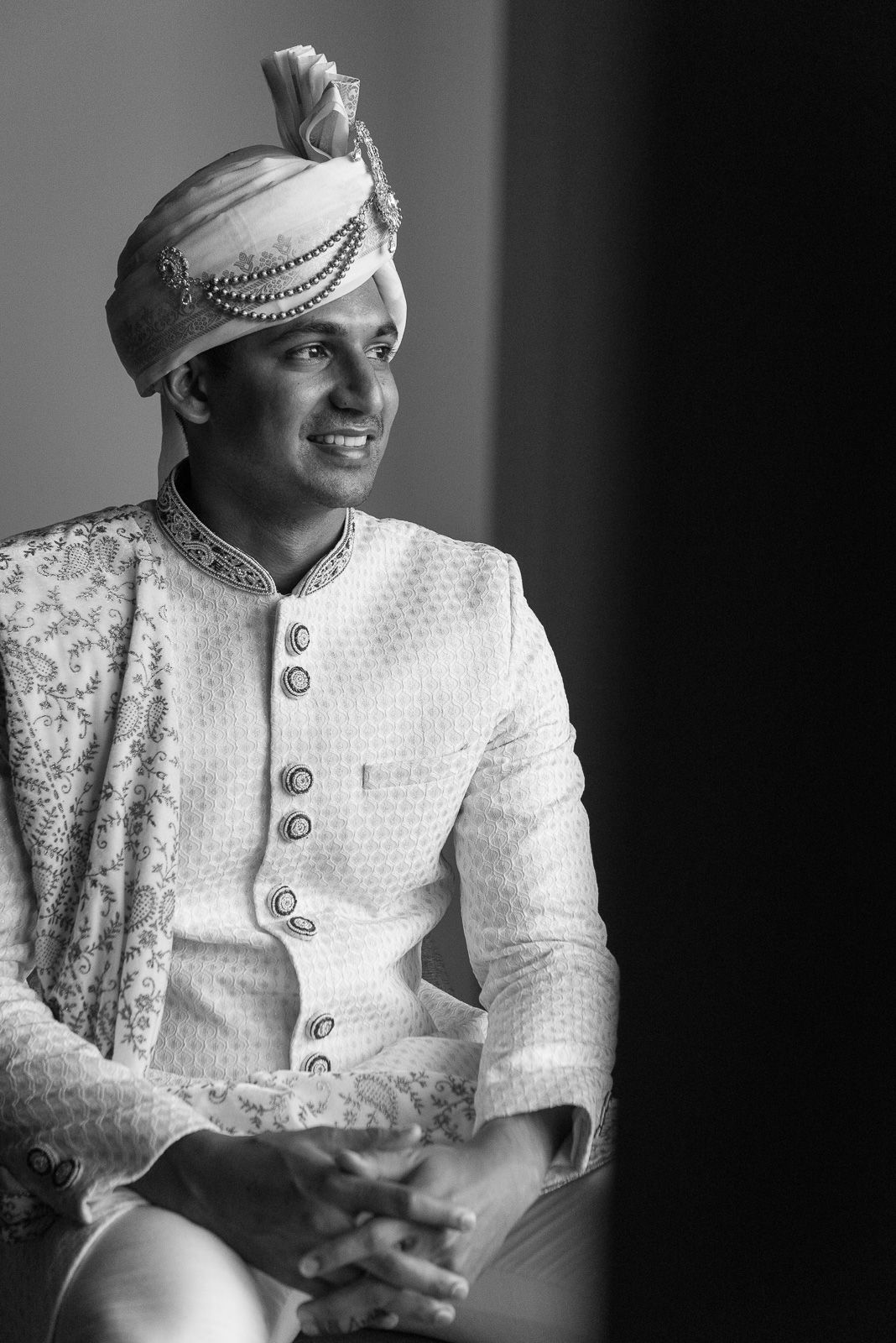Traditional Indian groom in white sherwani and turban photographed in classic black and white style.