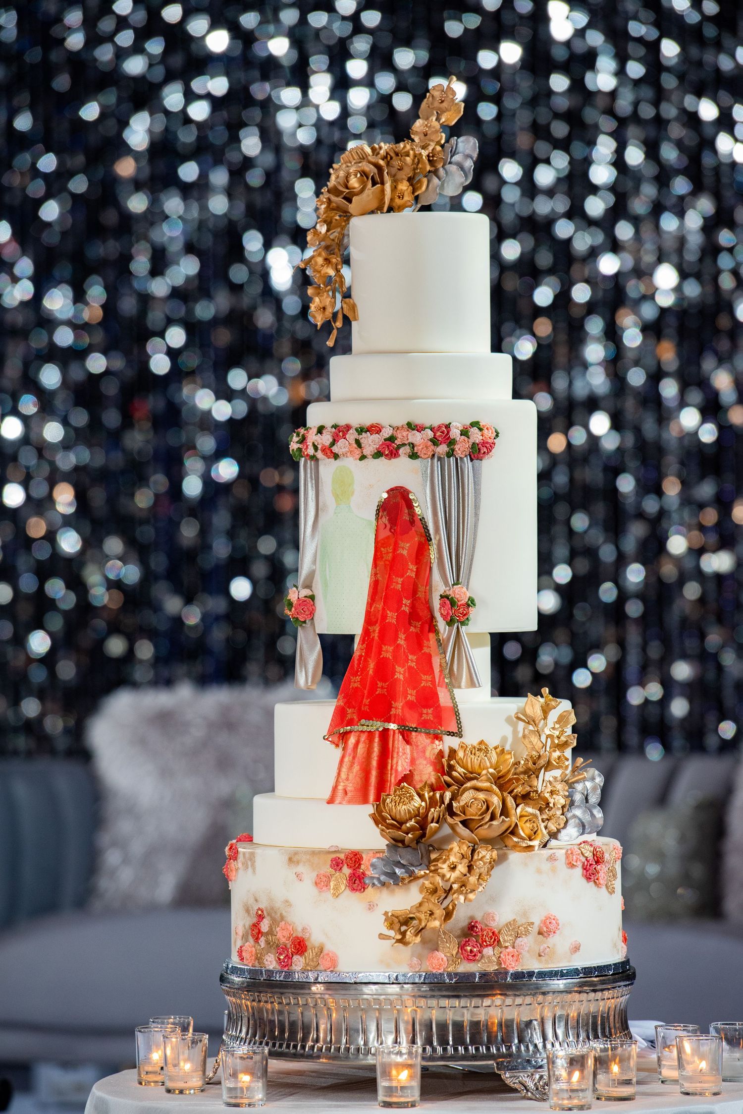 Elegant white wedding cake with gold accents and miniature red lehenga design detail.
