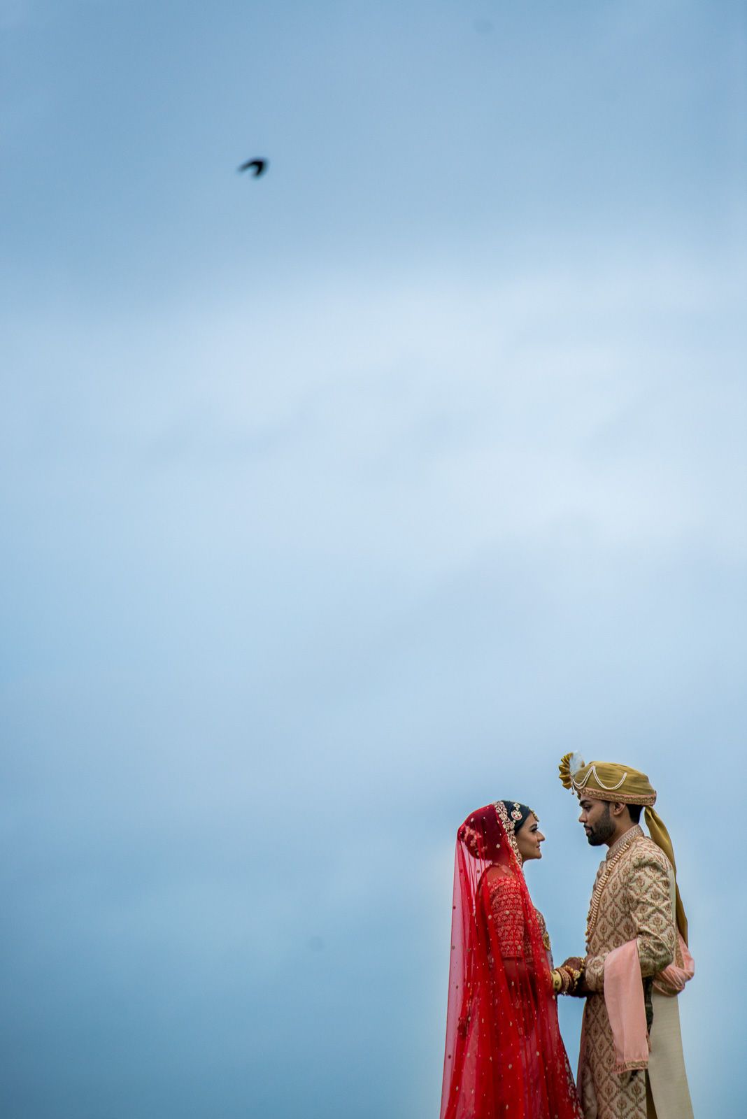 Traditional Indian wedding ceremony against blue sky with dramatic red bridal attire.
