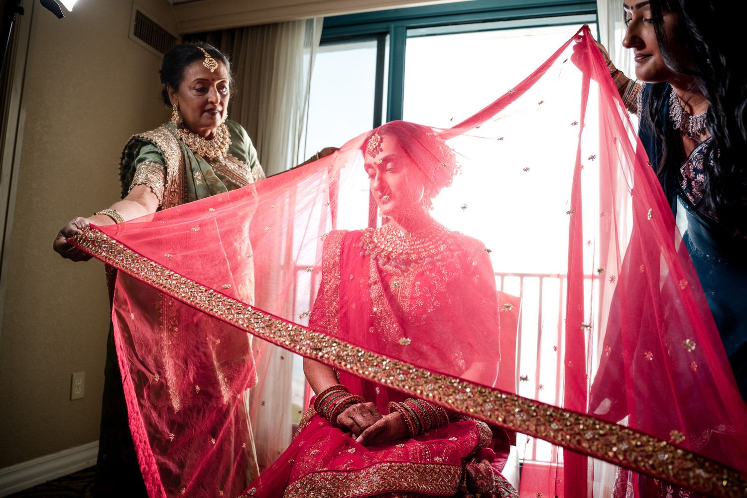 Wedding preparation scene with flowing red dupatta being draped in natural window light.