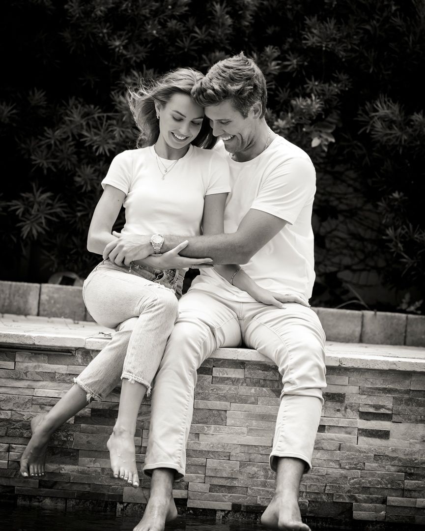 Tender moment between couple sitting on stone ledge in matching white outfits.
