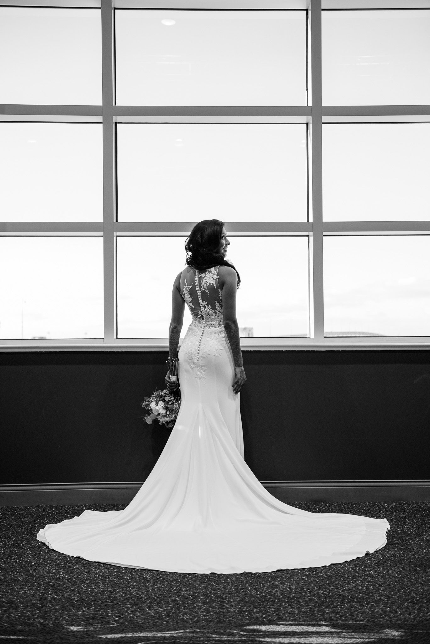 Silhouette of bride in fitted lace gown with dramatic train against large window.
