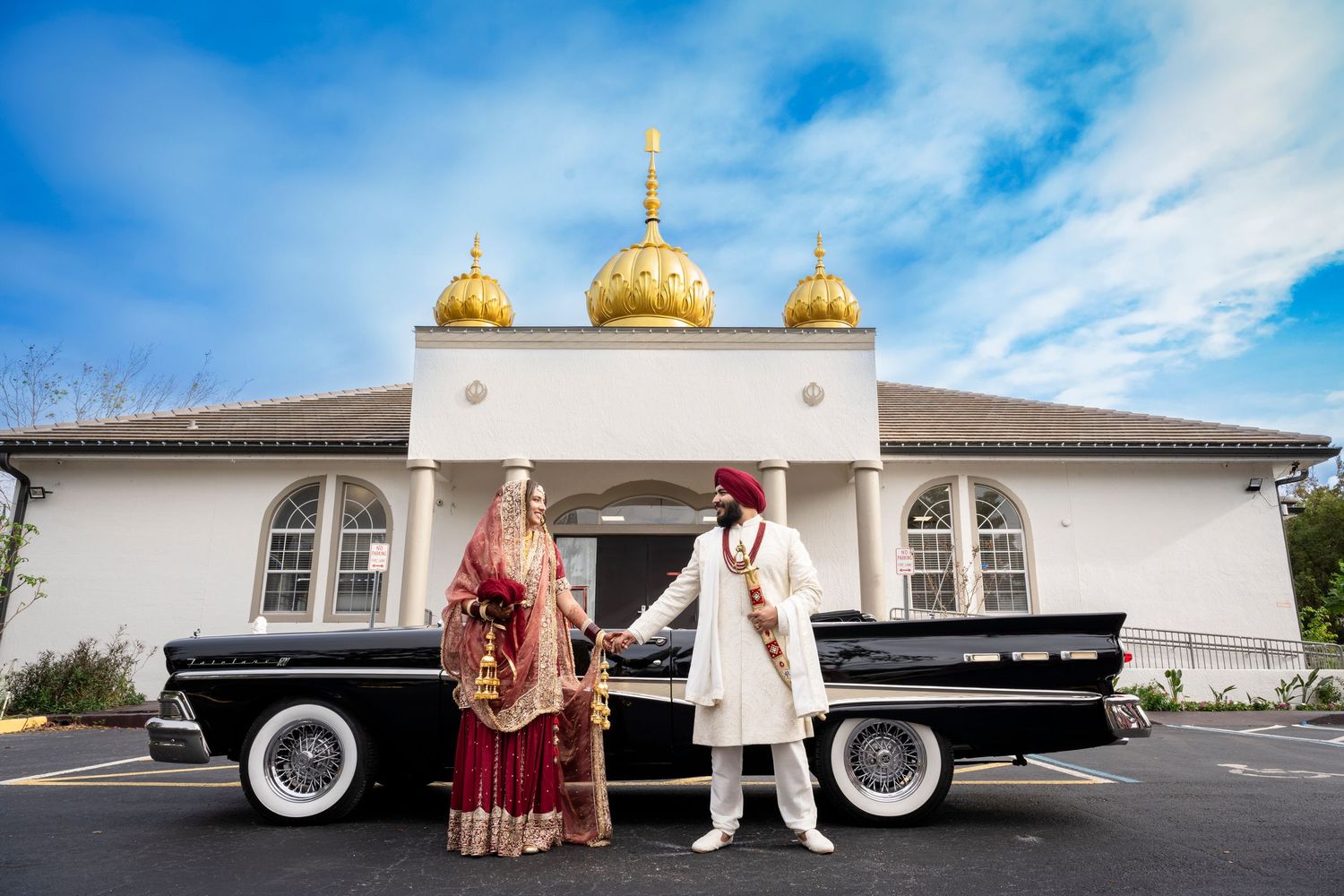 Wedding couple posed with vintage black car in front of temple with golden domes.