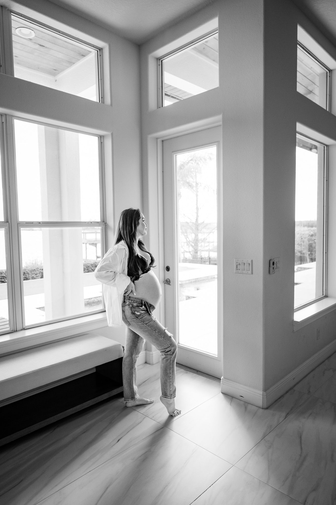 Silhouette of pregnant woman standing by large windows in modern interior.