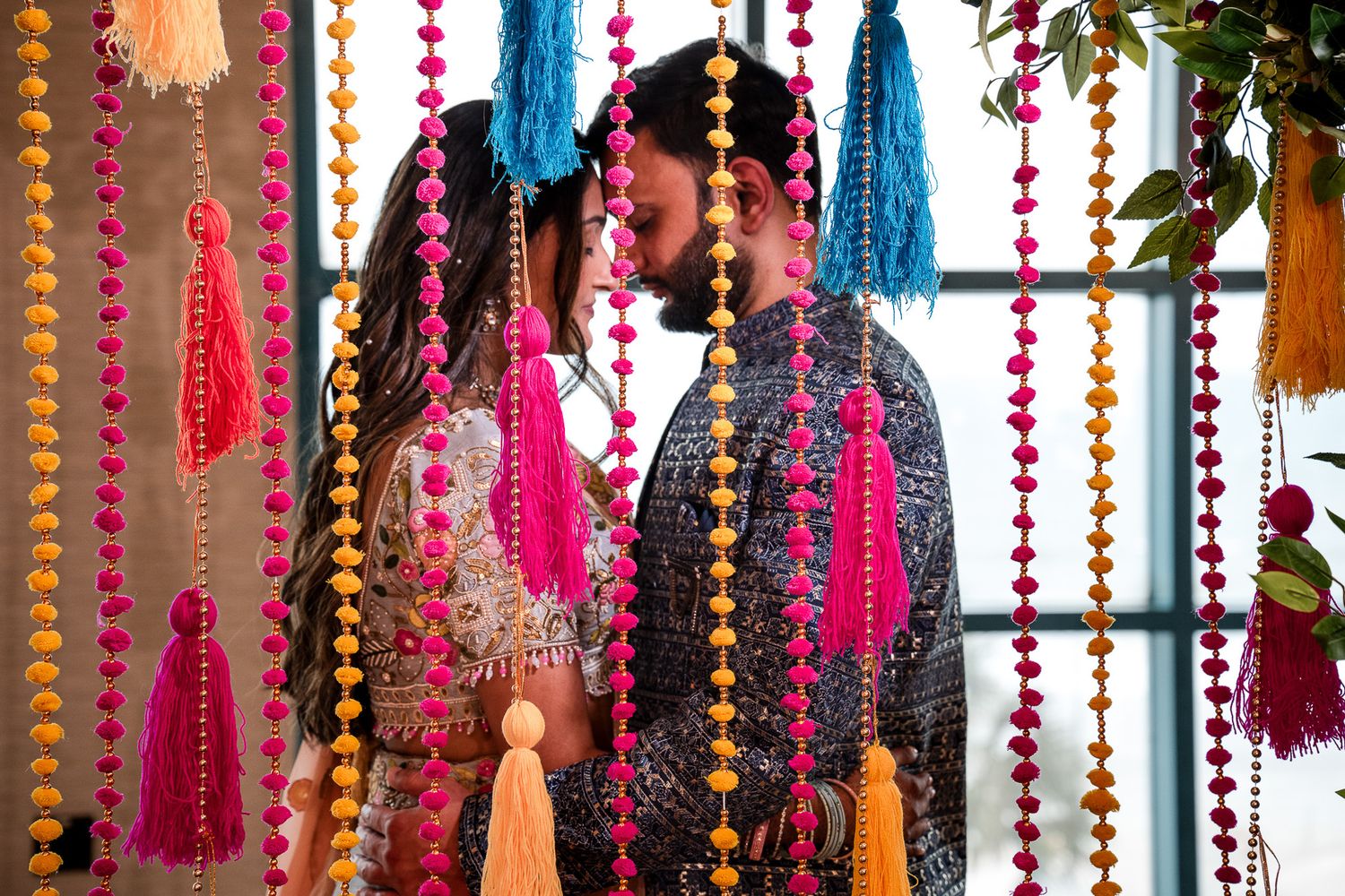 Colorful tassels and beaded decorations hanging against window at Indian wedding.
