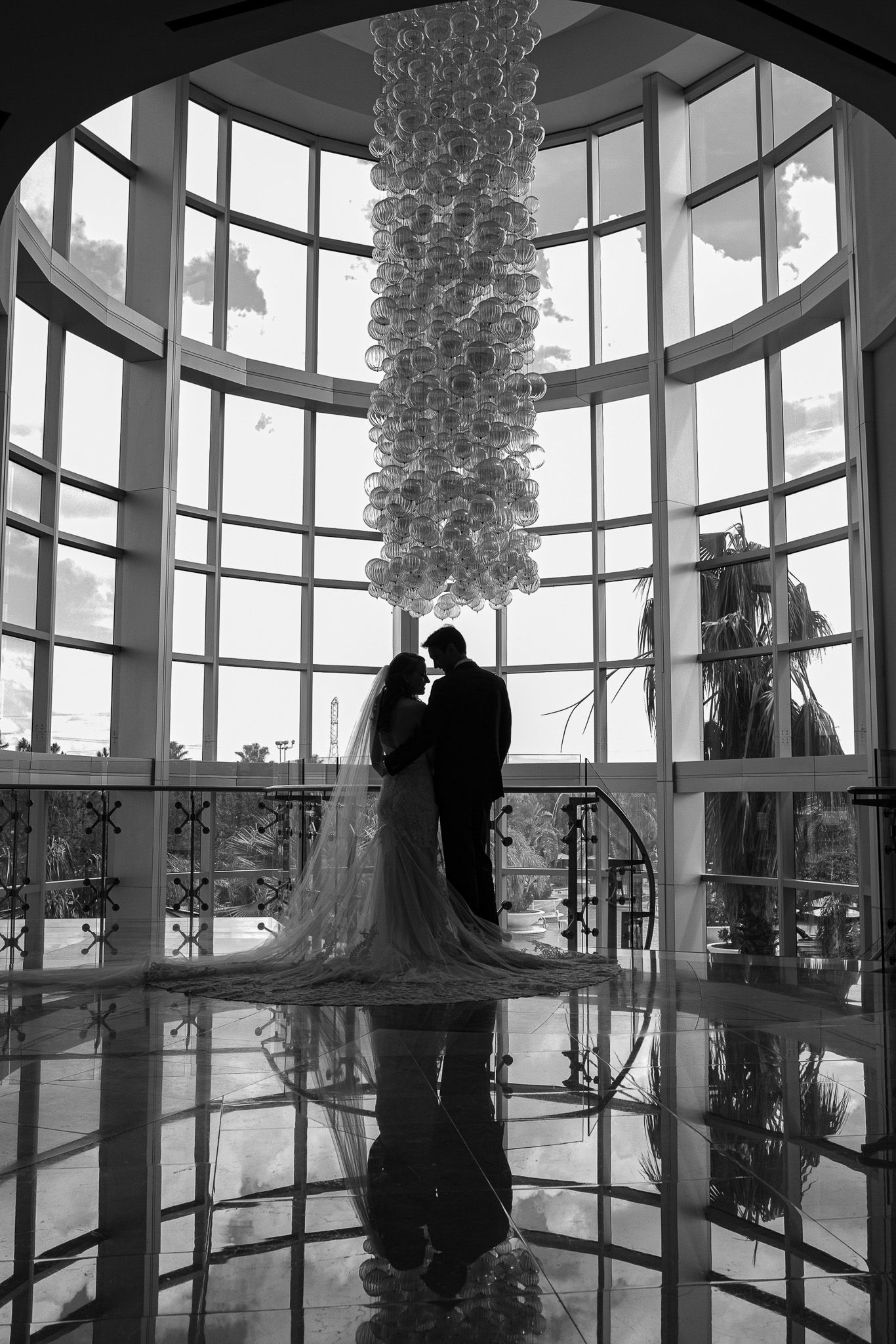 Silhouetted couple standing under dramatic glass atrium with hanging crystal chandelier.