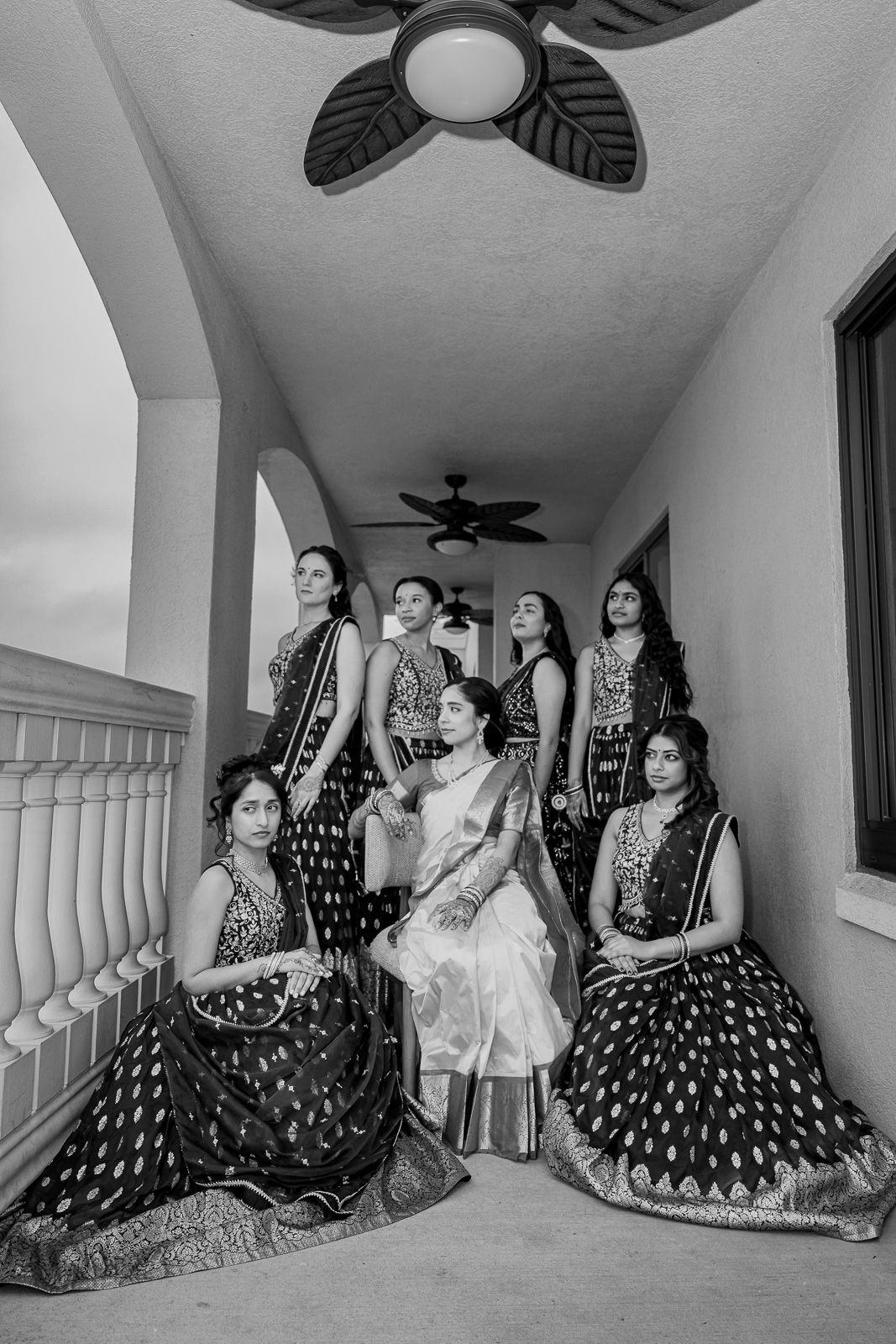 A group of women in traditional polka dot dresses pose together on a covered balcony.