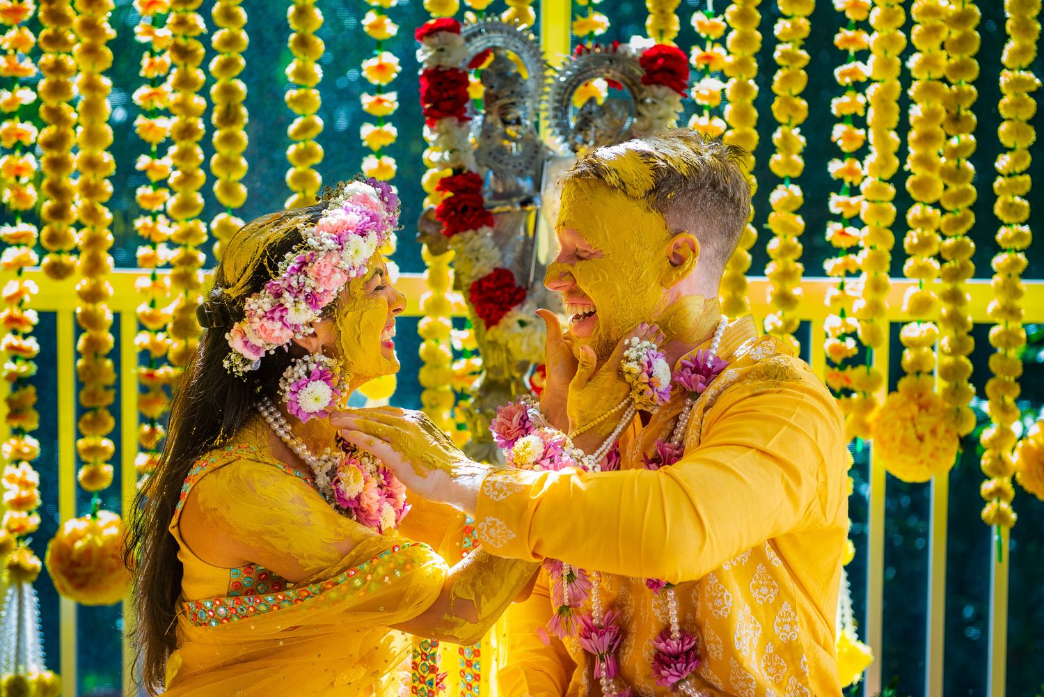 Couple celebrating a traditional Indian Haldi ceremony with yellow turmeric and flower decorations.