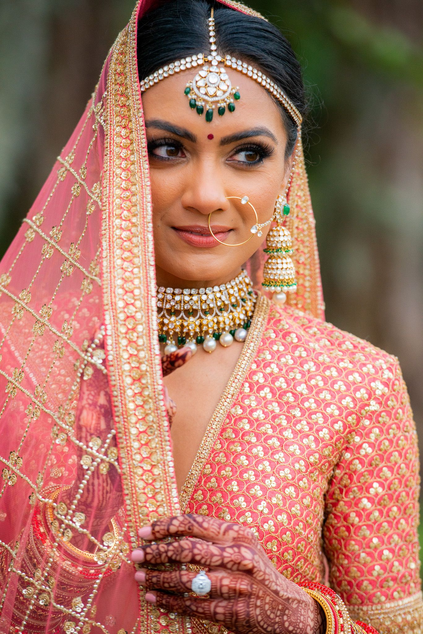 Traditional Indian bride wearing coral pink lehenga with ornate gold jewelry and headpiece.