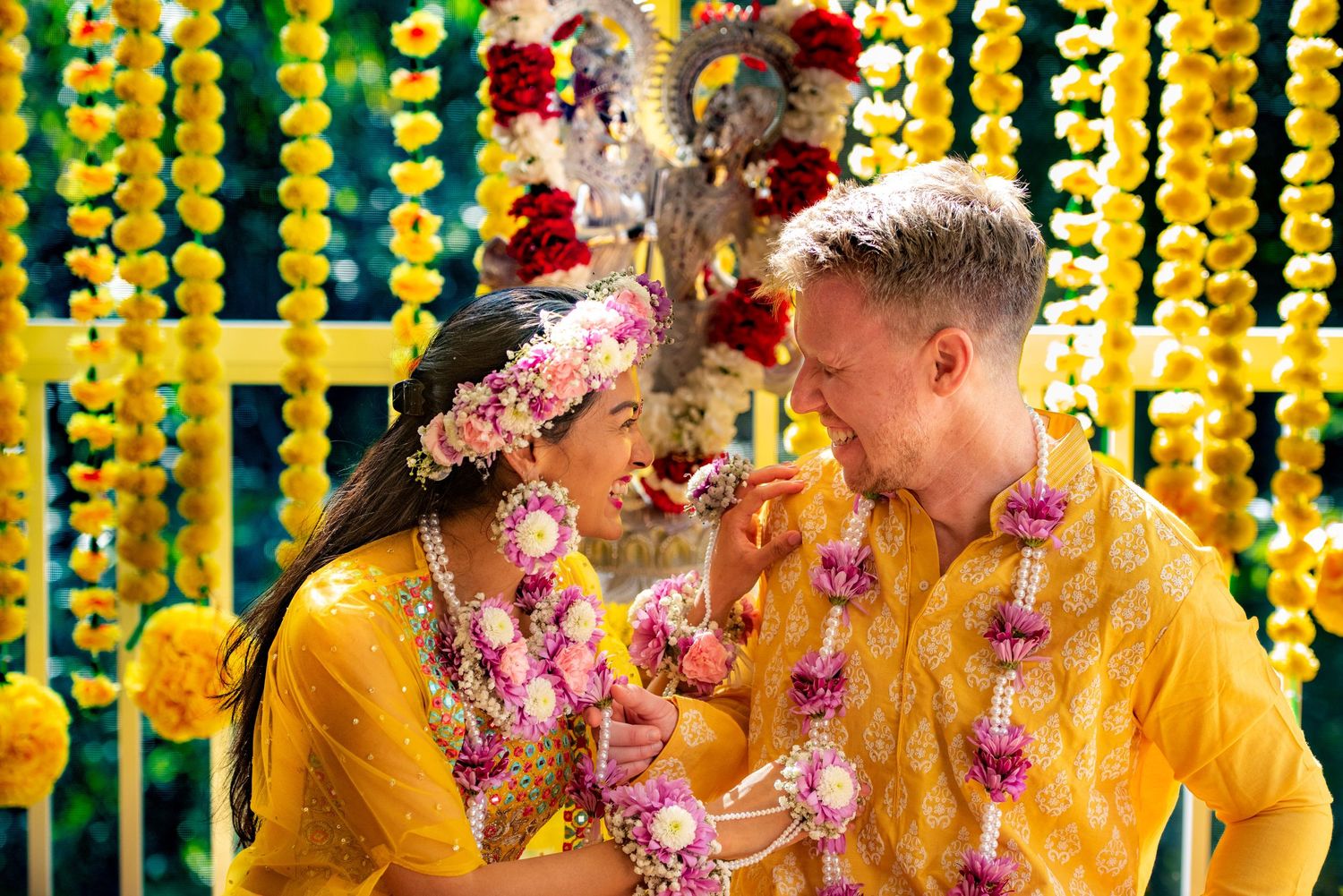 Couple wearing yellow traditional outfits and flower garlands share intimate moment.