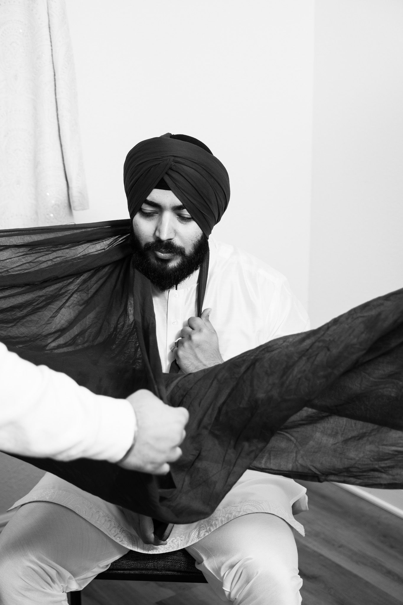 Black and white portrait of a man adjusting his traditional Sikh turban.