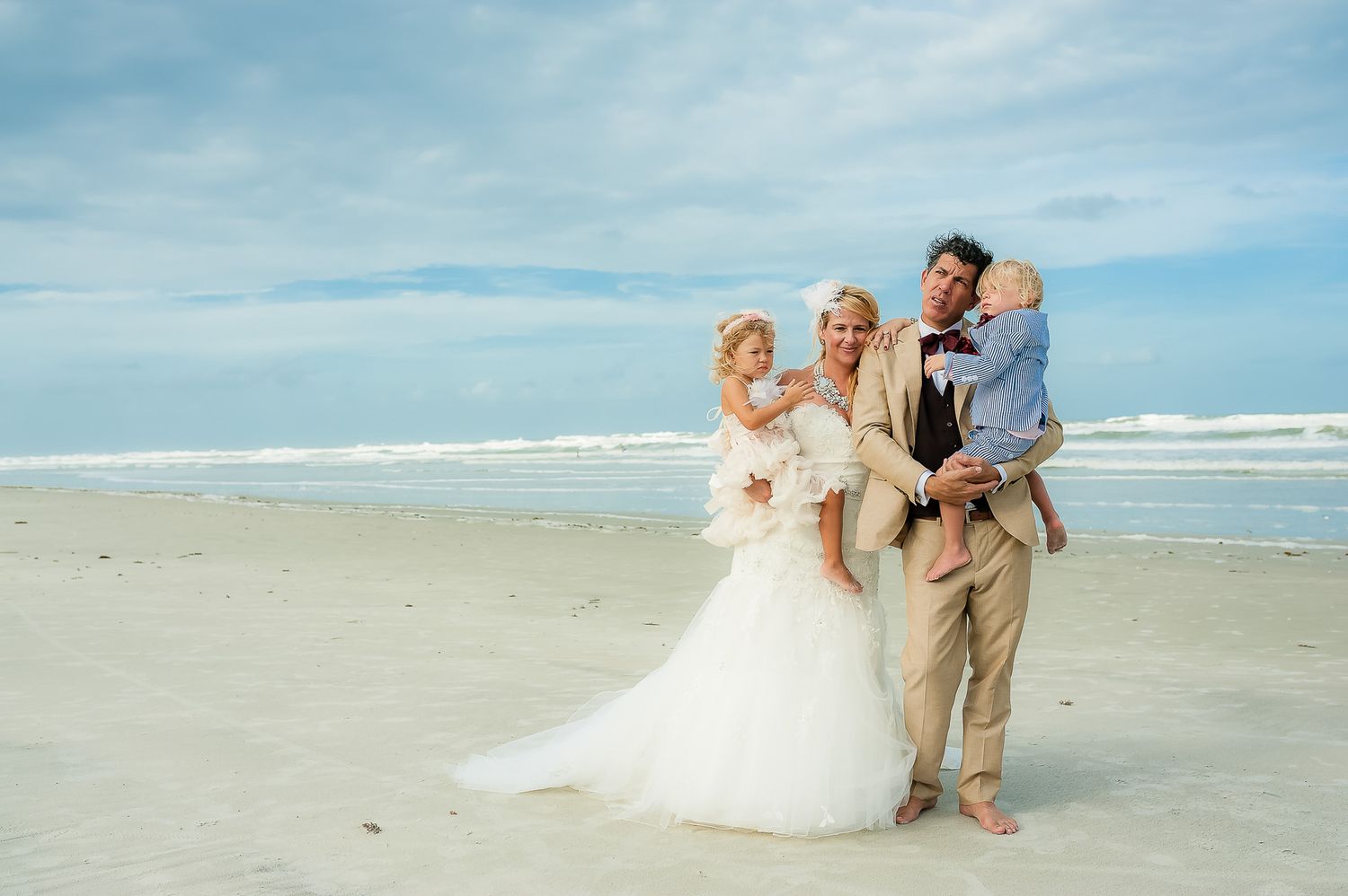 Family celebrates together on sunny beach in wedding attire.