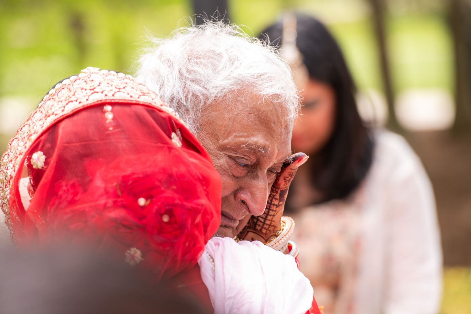 Person wearing red bandana smelling flower in outdoor setting.