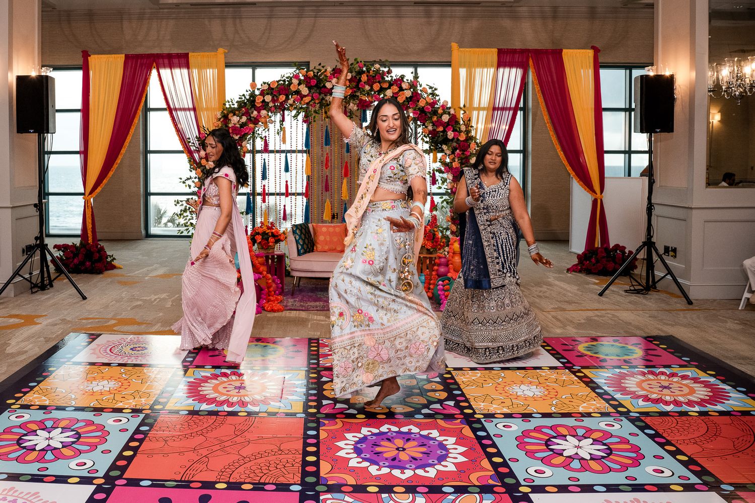Traditional Indian wedding celebration with colorful rugs and floral arch decorations.
