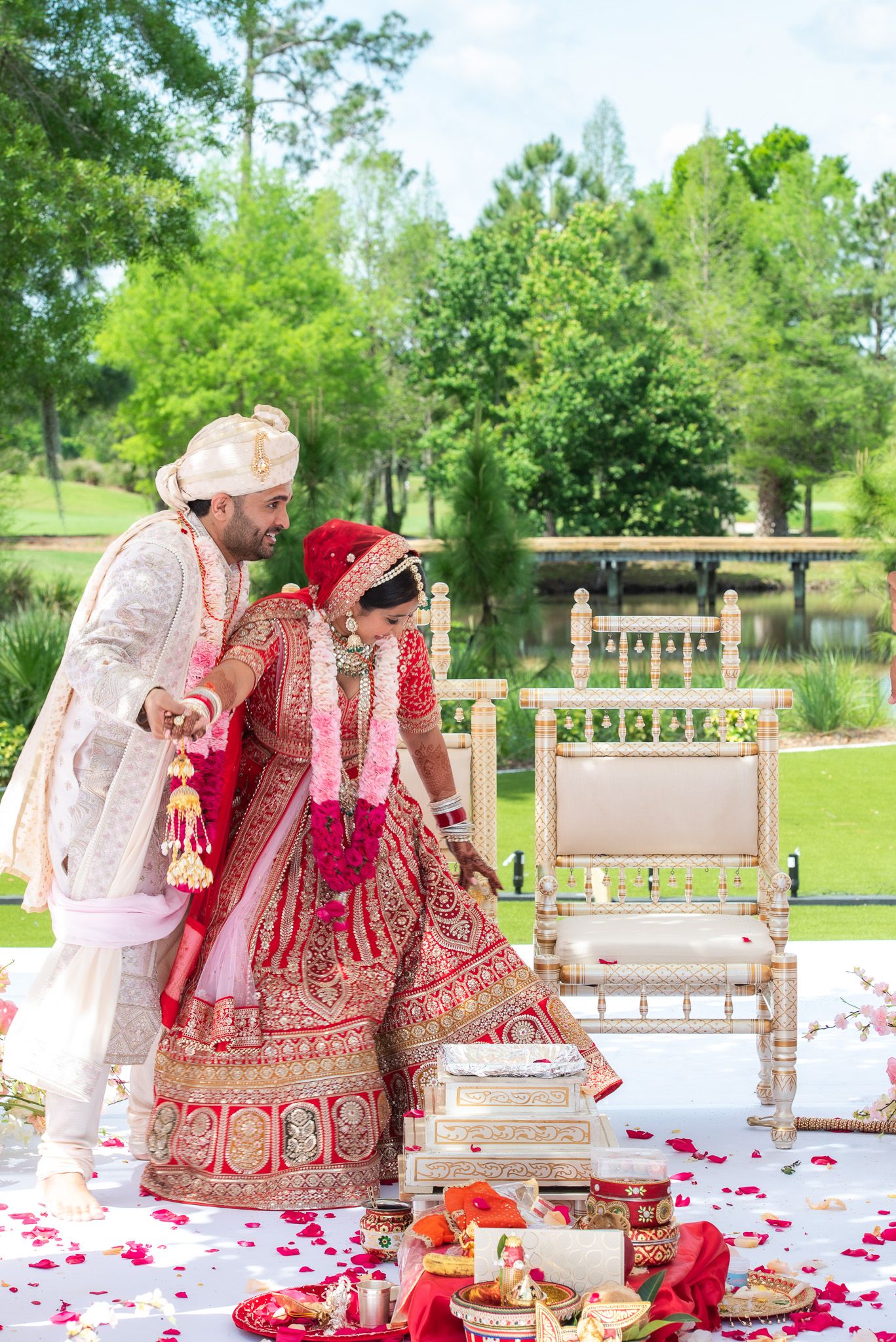 Traditional Hindu wedding ceremony with couple performing rituals on decorated outdoor stage with rose petals.