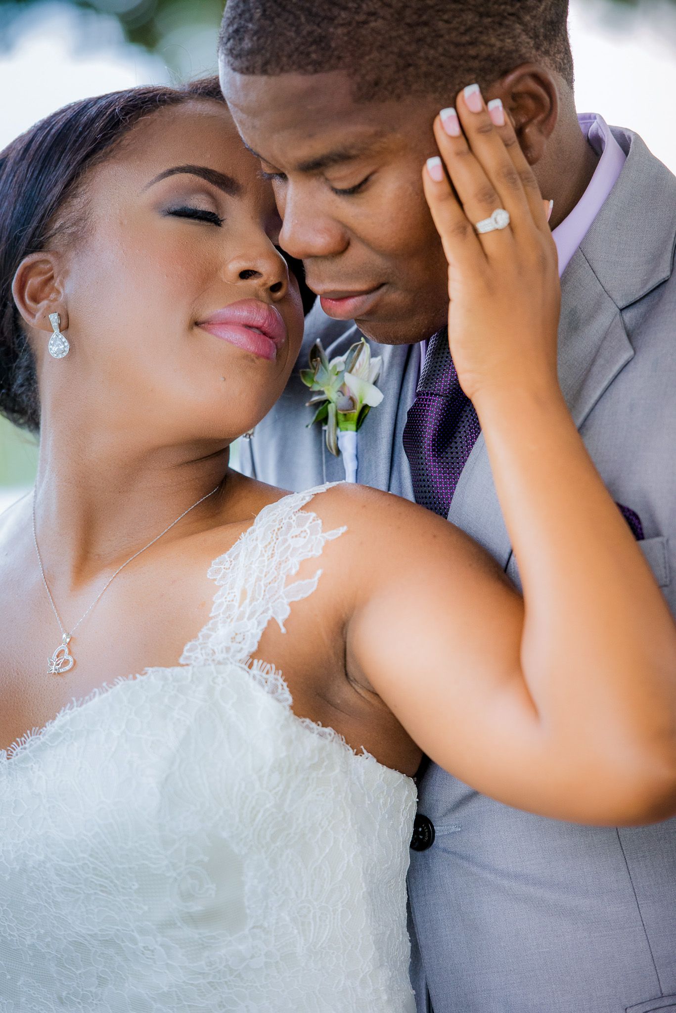 Intimate moment between newlyweds as bride caresses groom's face, showing off engagement ring.