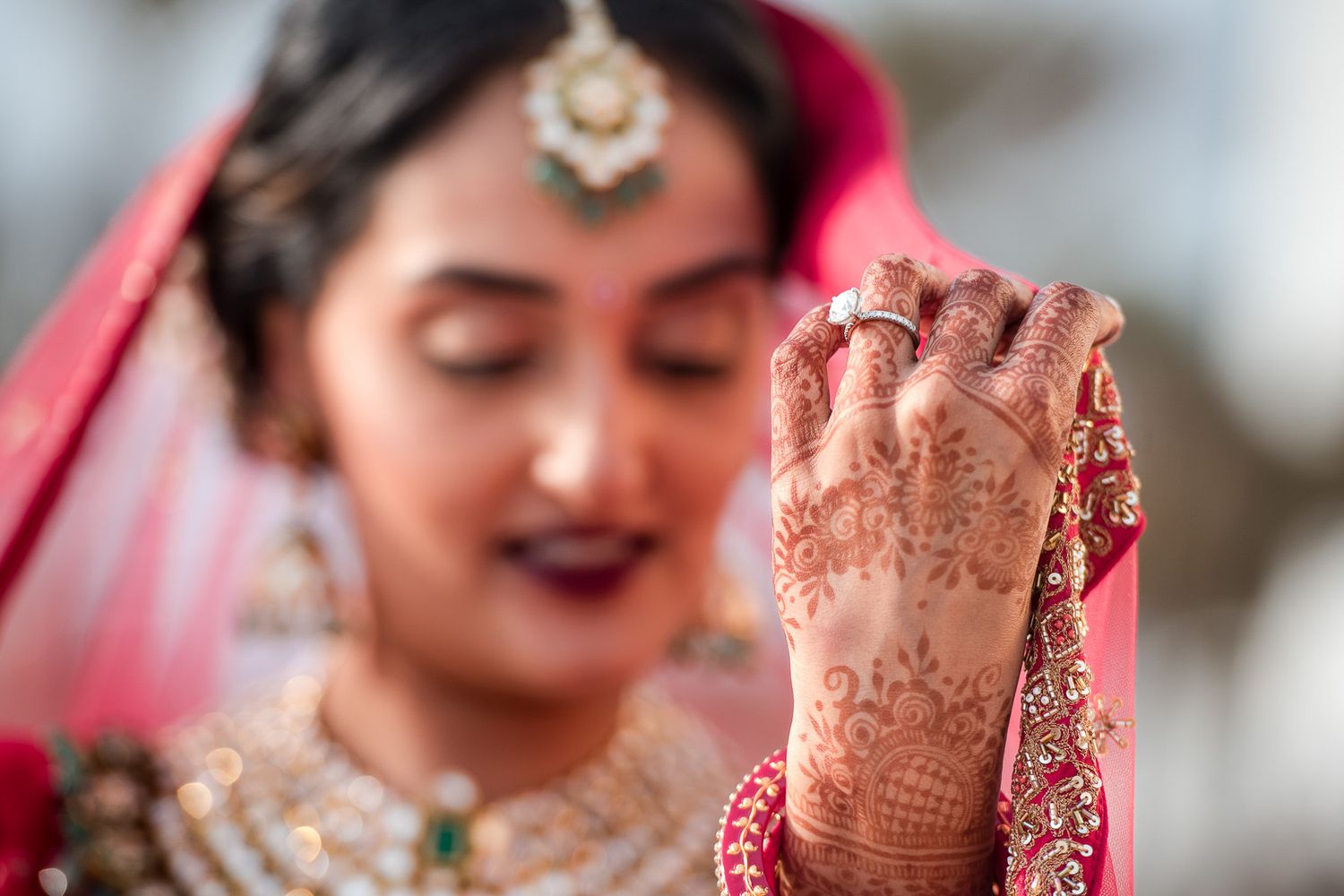Detail shot of traditional henna design on hands with jewelry and red bridal attire.
