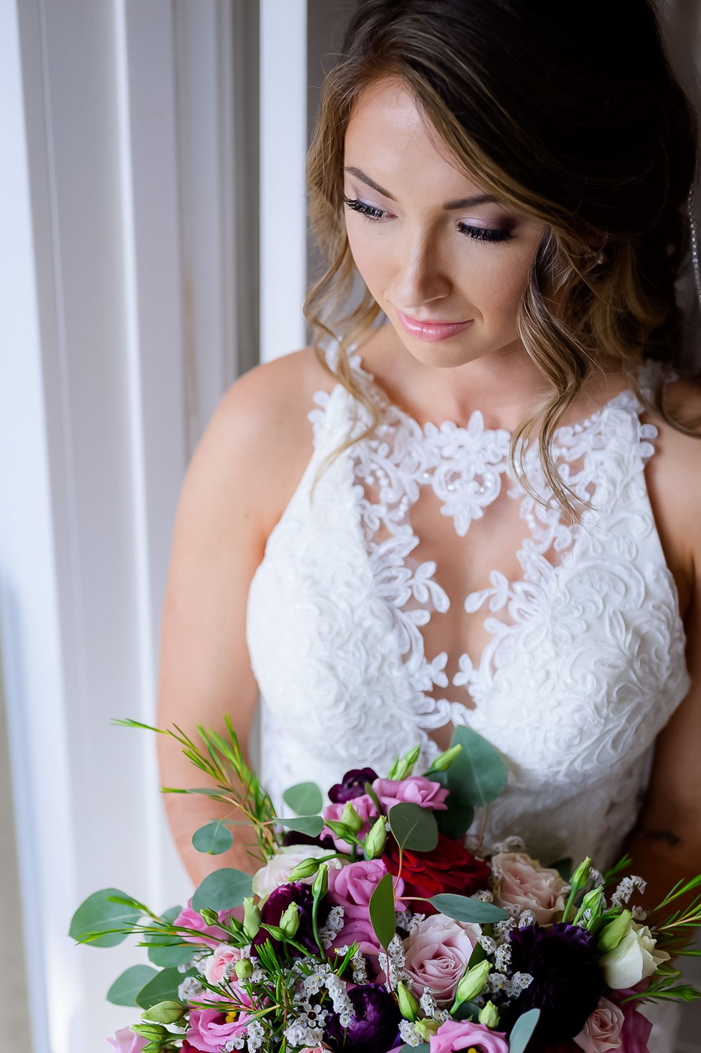 Bride in lace wedding dress holding colorful bouquet of pink and purple flowers with greenery.
