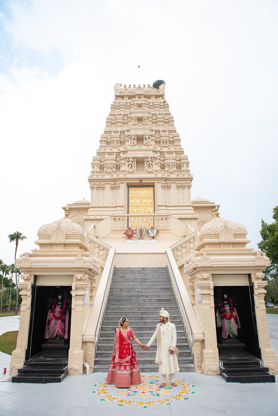 Traditional Indian couple standing at ornate temple entrance decorated with flower petals.