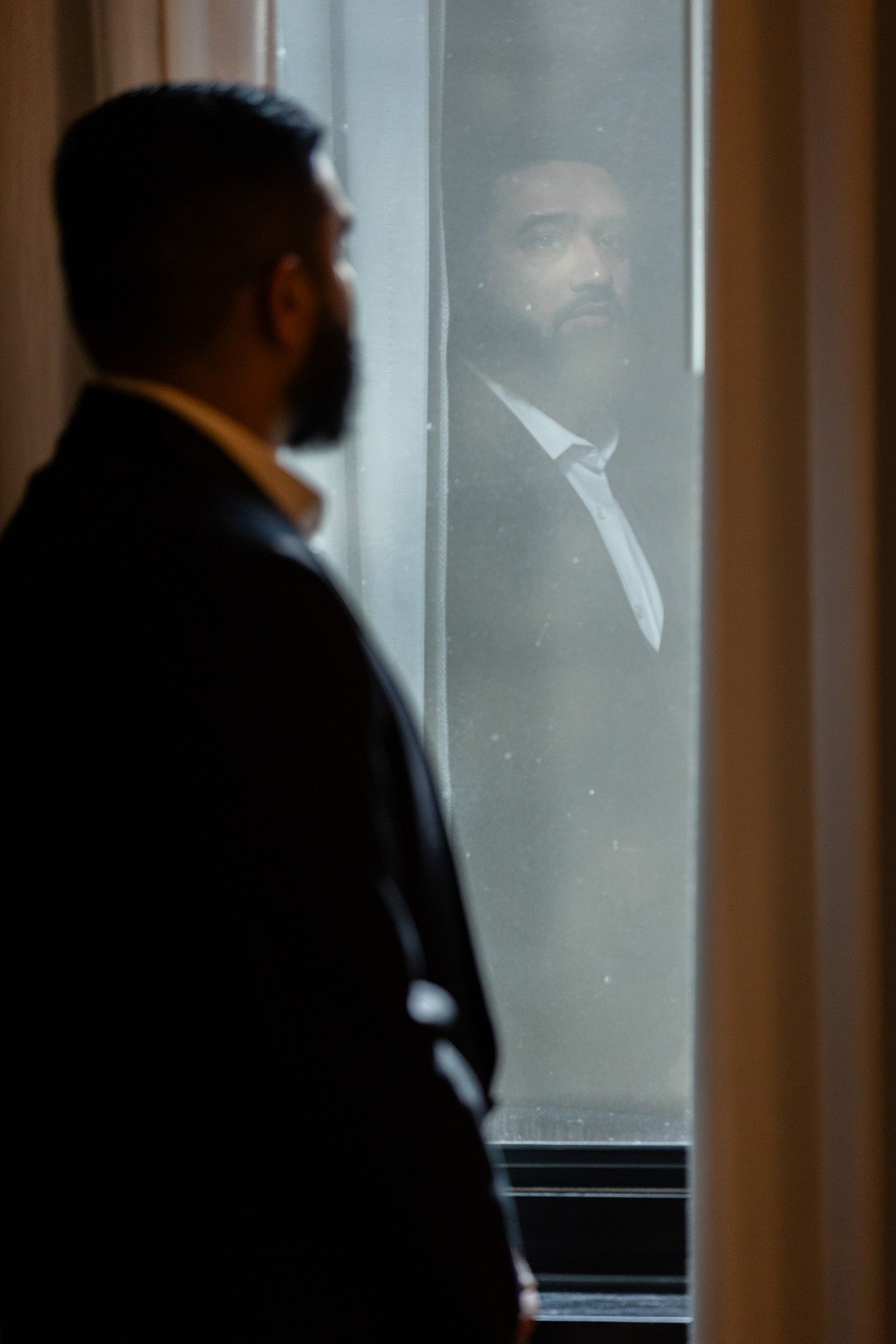 Dramatic silhouette of suited figure looking through window reflection.