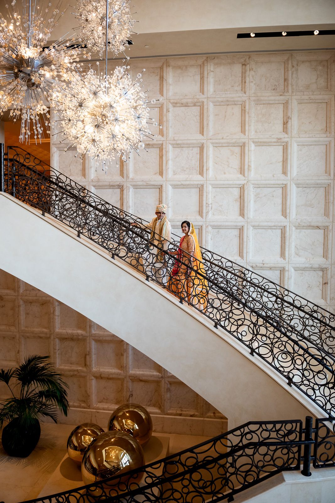 Grand staircase with ornate railing and crystal chandelier in luxury wedding venue.