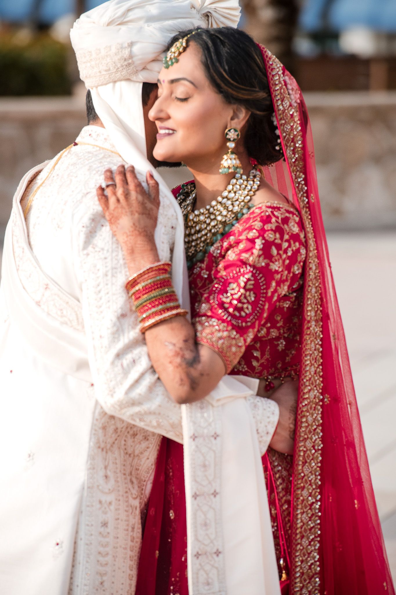 Intimate moment between newlyweds wearing traditional Indian wedding attire with bride in red lehenga.