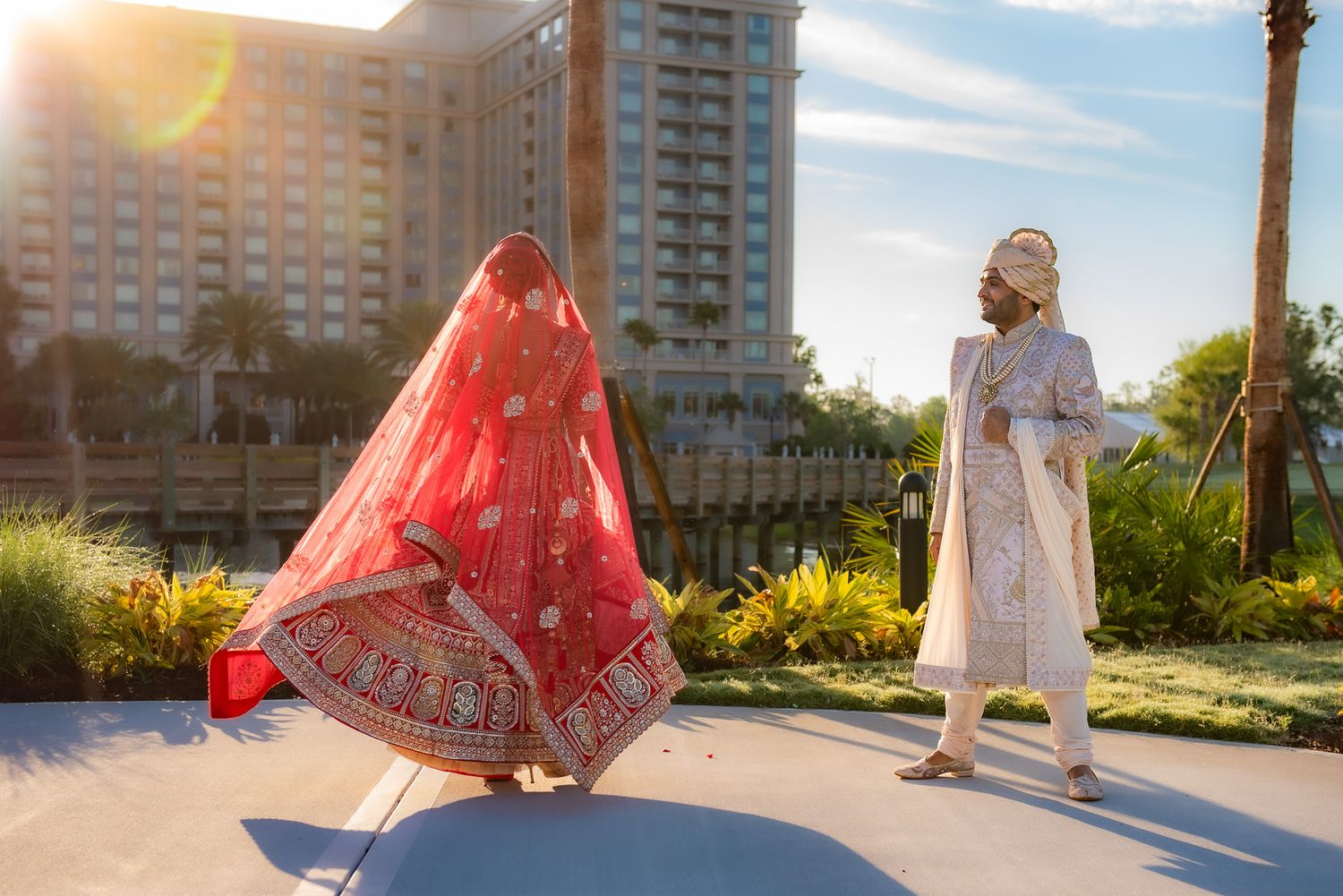 Bride in red lehenga twirling outdoors with cityscape in background.