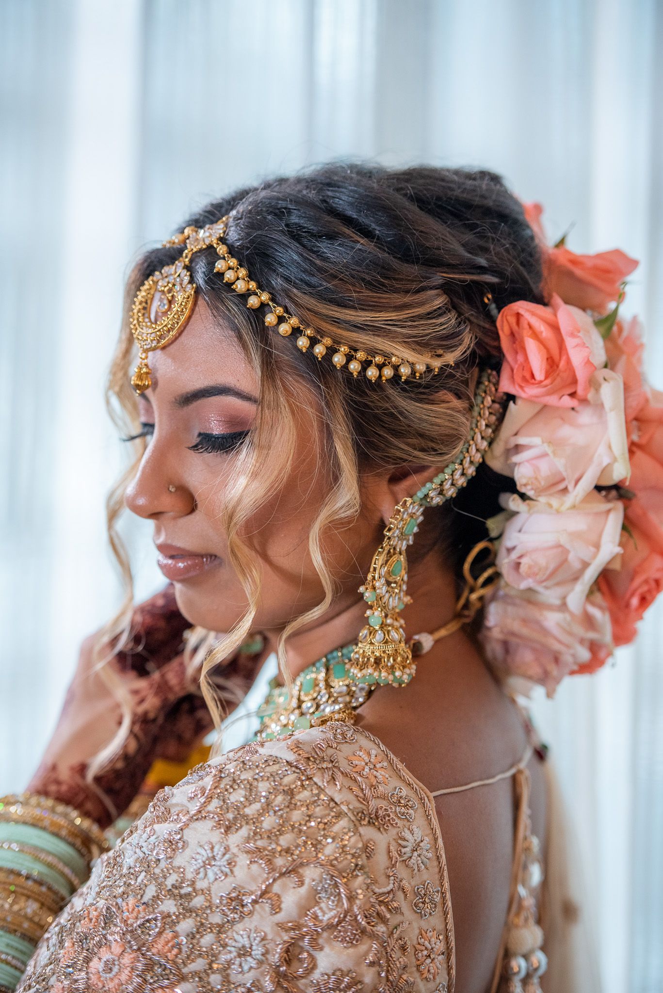 Profile view of a bride wearing ornate gold headpiece and peach flowers in her hair.