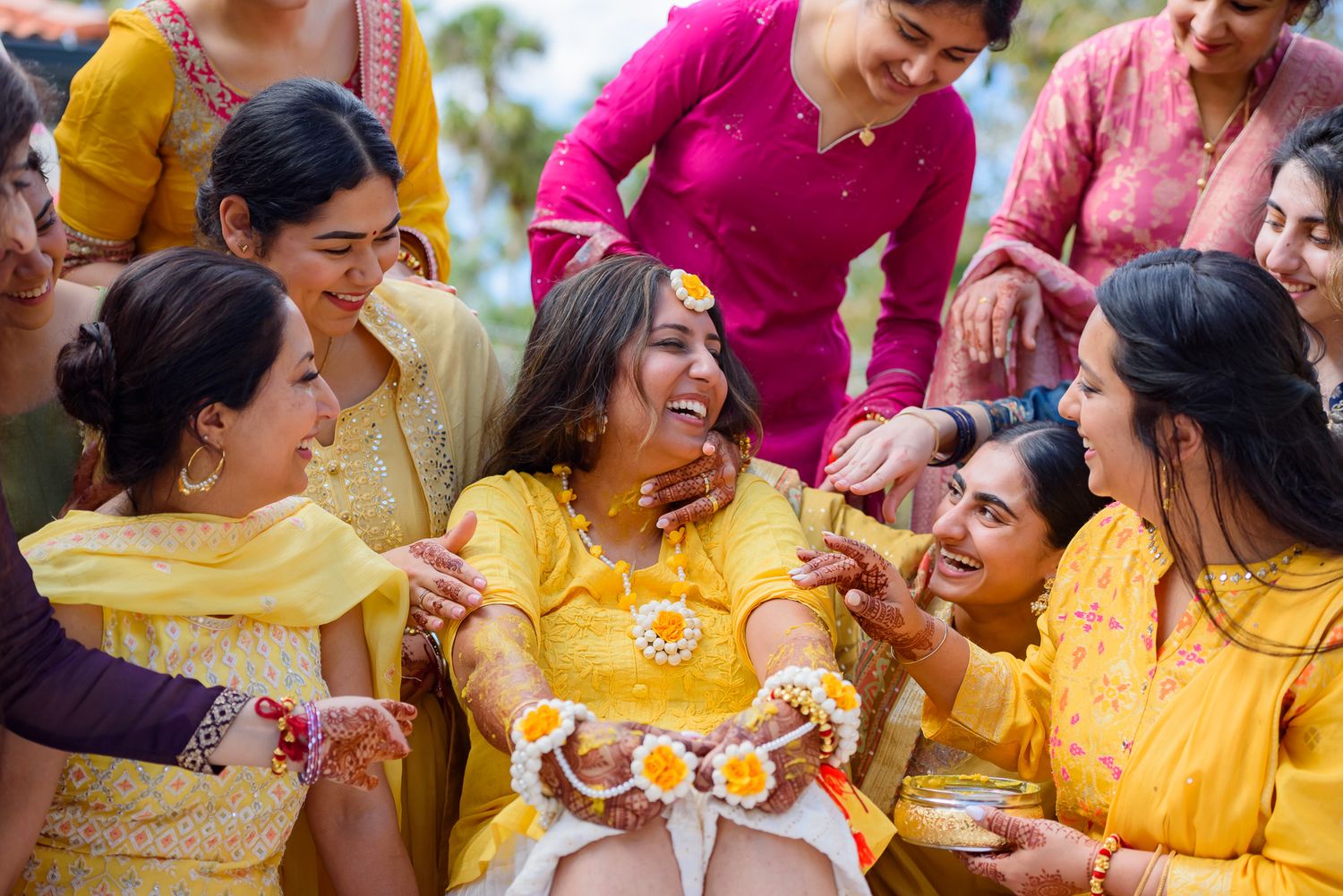 Joyful celebration with women in bright yellow and pink traditional attire during a cultural ceremony.