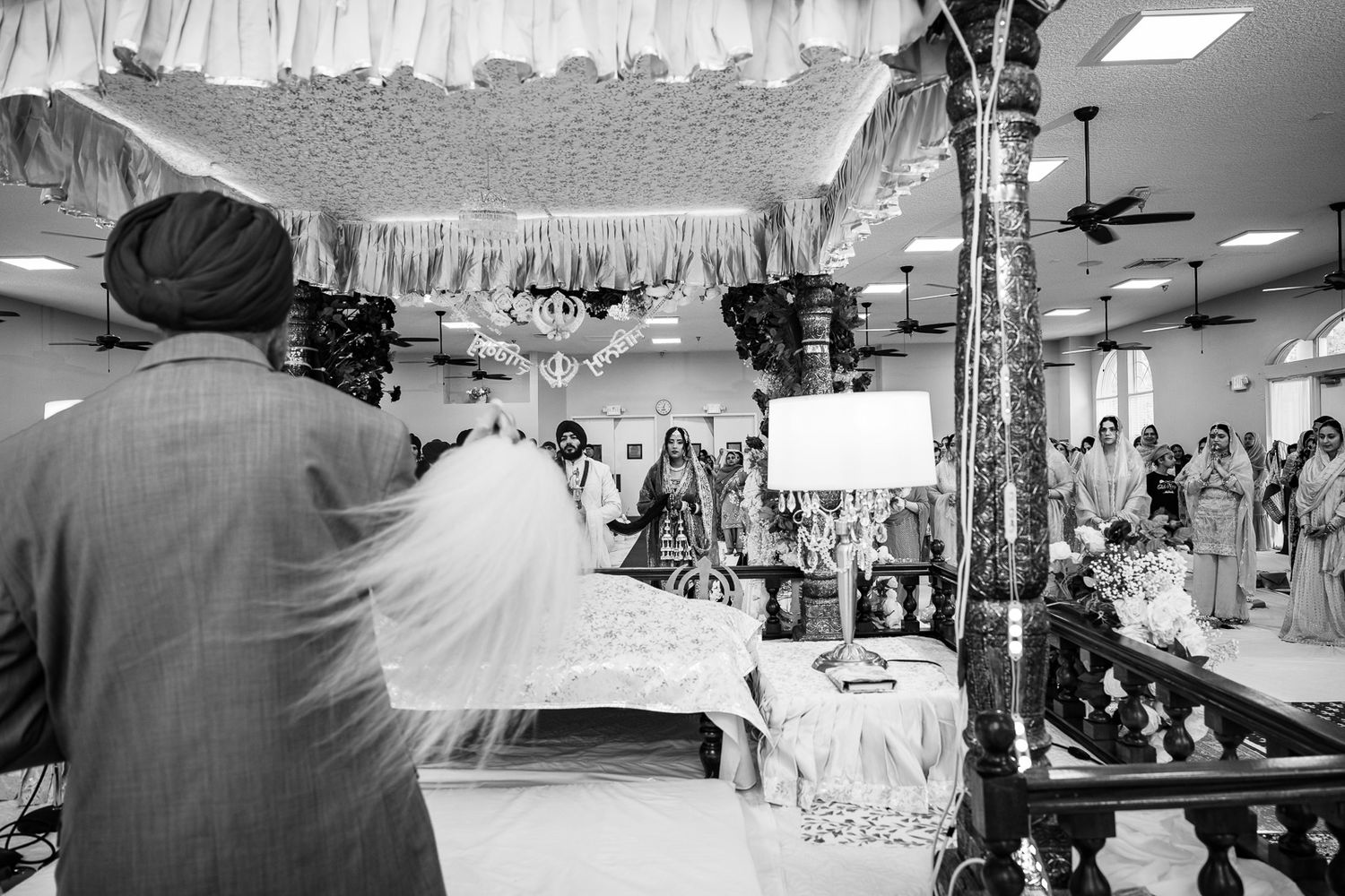 Black and white photo of wedding preparation scene with hanging decorations and busy atmosphere.