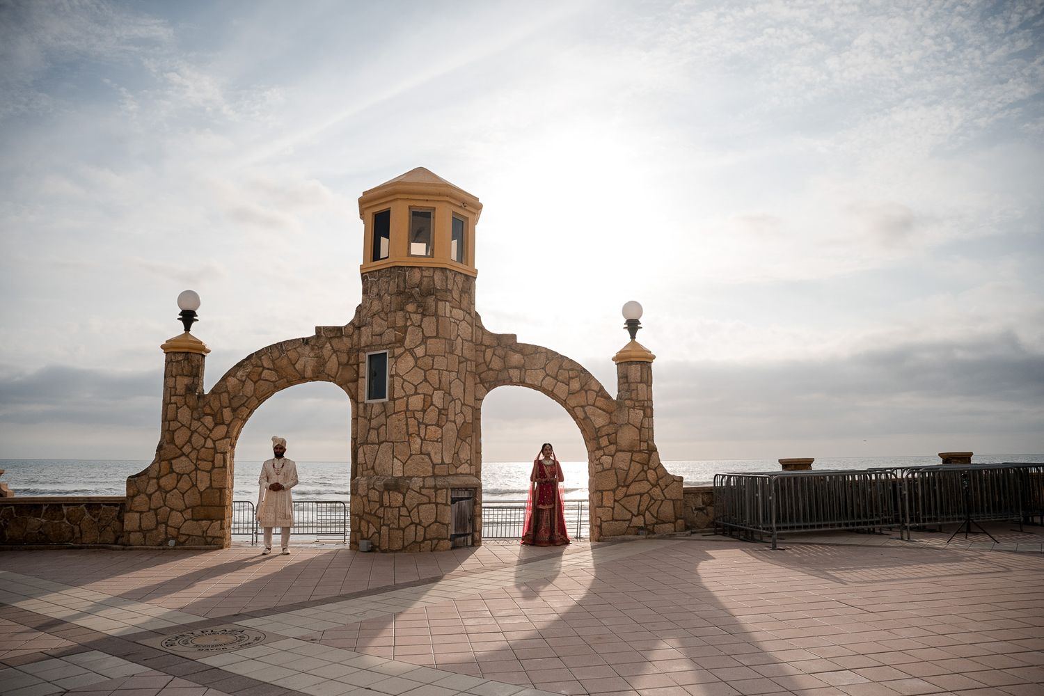 Stone archway with tower creates silhouette of couple in traditional wedding attire.