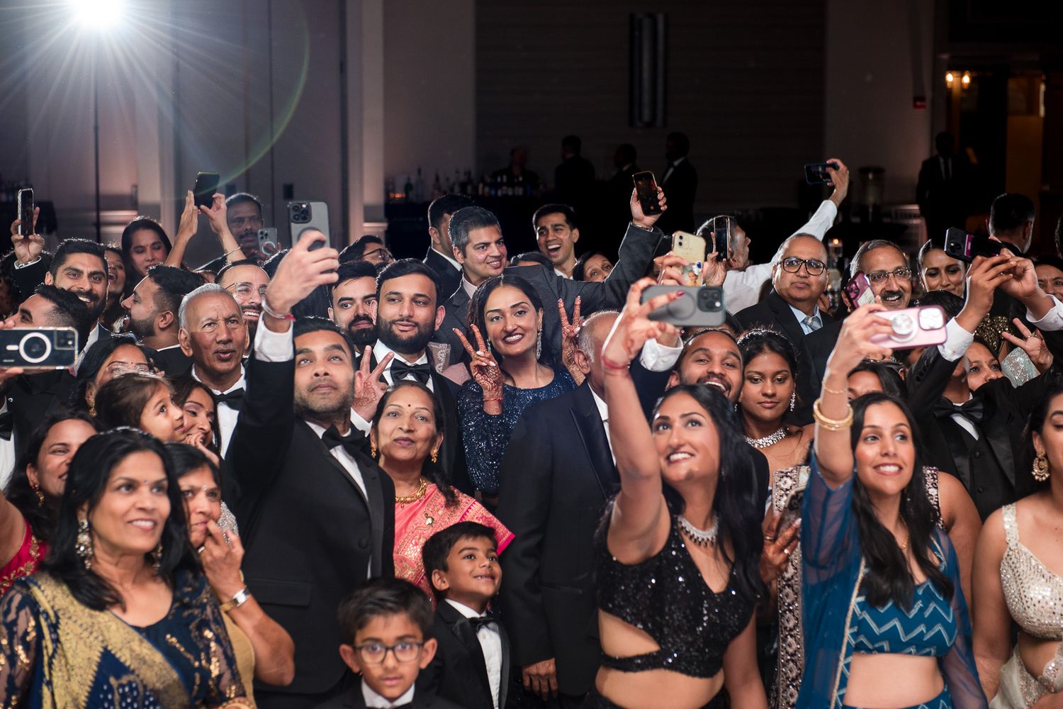Energetic crowd of formally dressed guests celebrating and taking photos at an event.