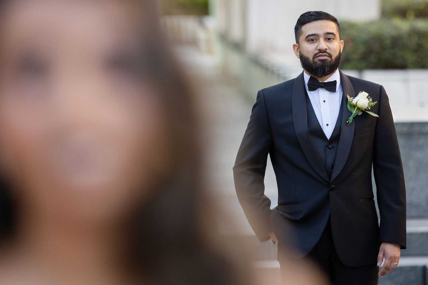 Groom in tuxedo and boutonniere poses in selective focus portrait.