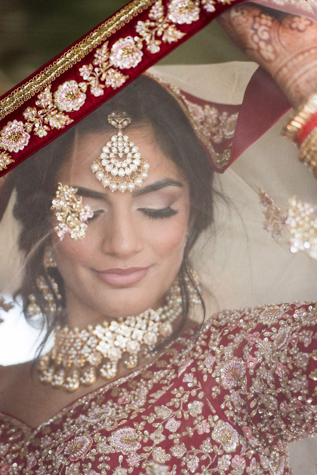 Close-up portrait of traditional Indian bridal jewelry and embroidered red fabric with intricate details.