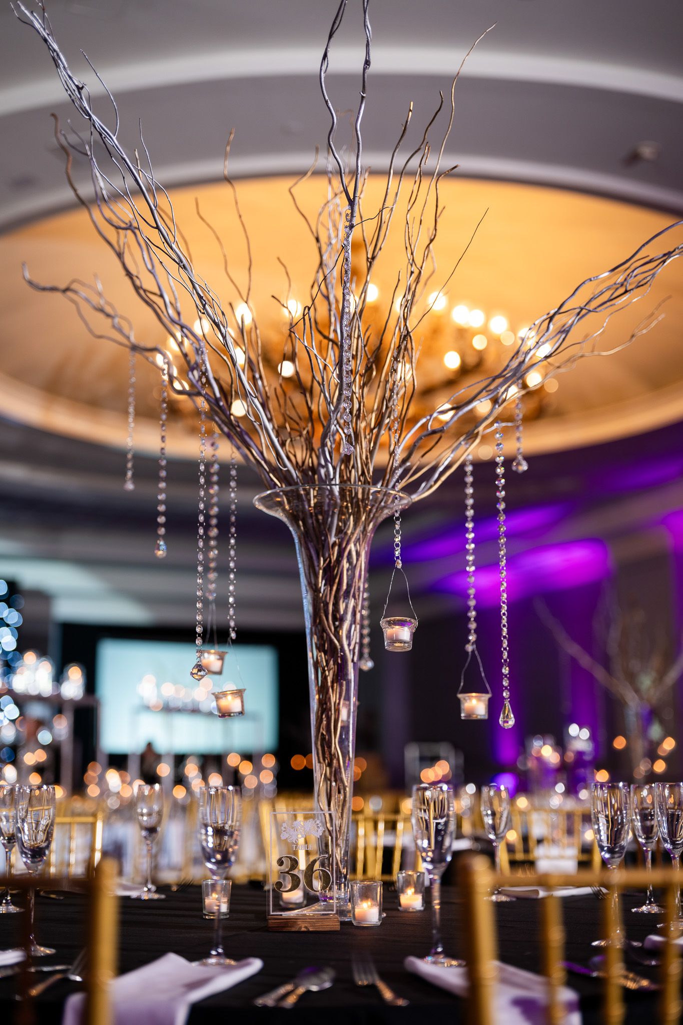 Elegant centerpiece with crystal-draped branches and candle holders on a formal table setting.