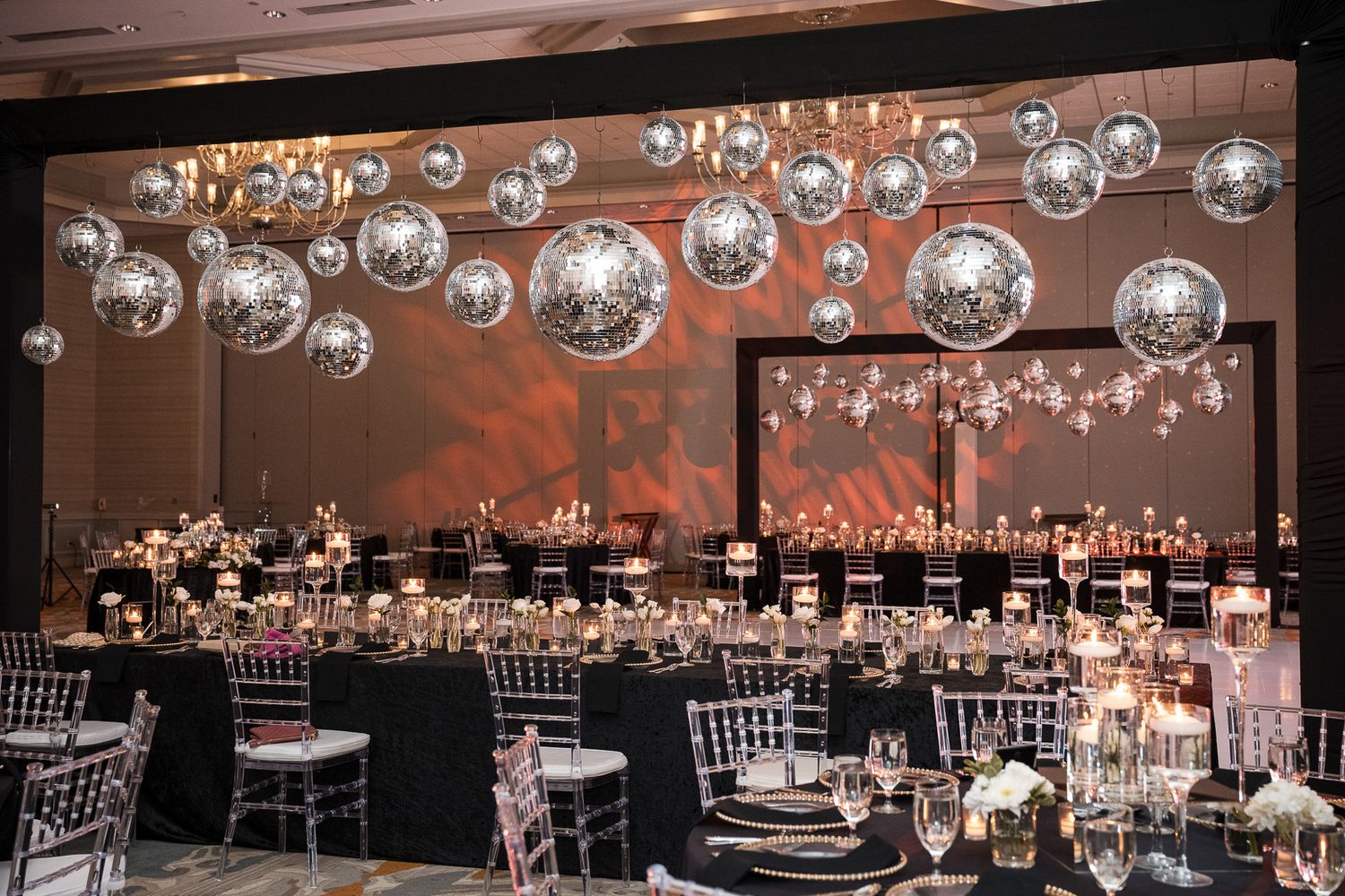 Luxurious reception decor featuring suspended disco balls over elegant table settings.