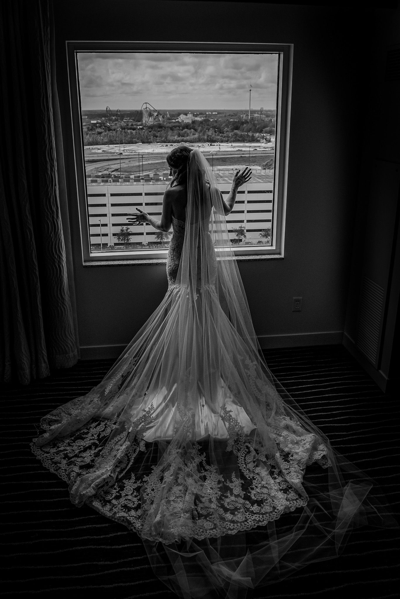 Dramatic black and white silhouette of bride in cathedral veil looking through window.