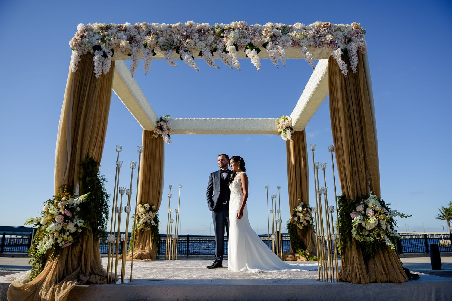 Wedding ceremony setup featuring a white draped arch with florals overlooking the water.