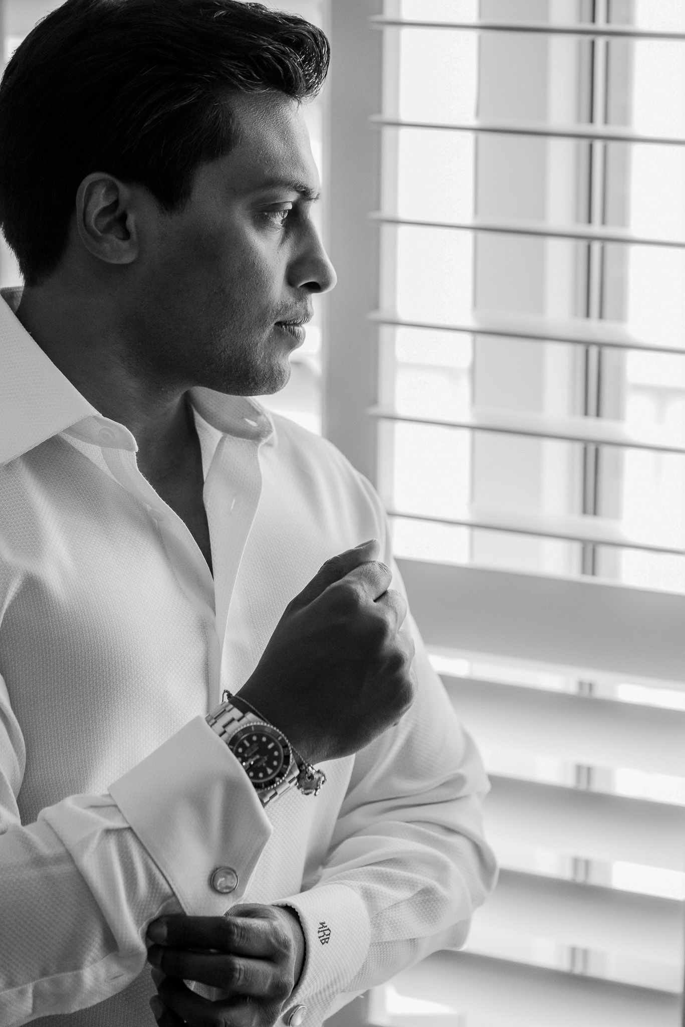 Black and white profile portrait of person adjusting formal white shirt cuff.