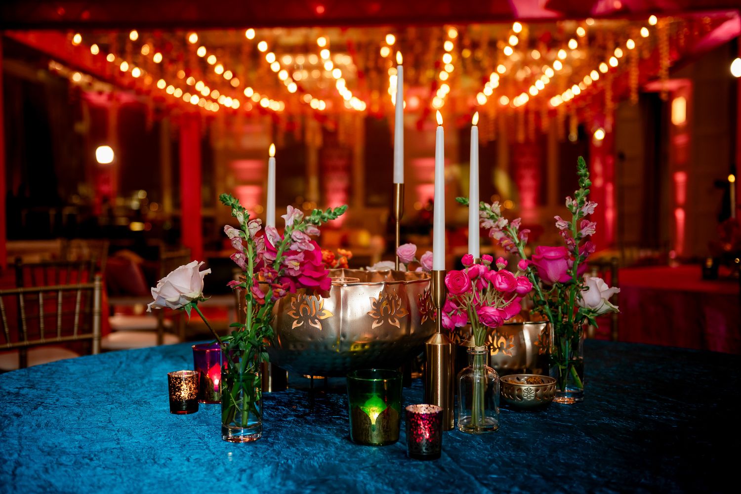 Wedding reception table decor with vibrant flowers and warm lighting against blue tablecloth.