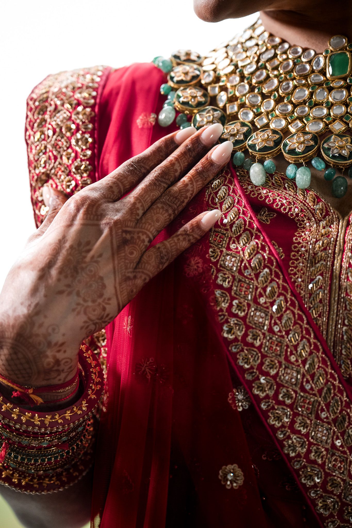 Detailed shot of hands with henna touching ornate kundan necklace with turquoise accents.
