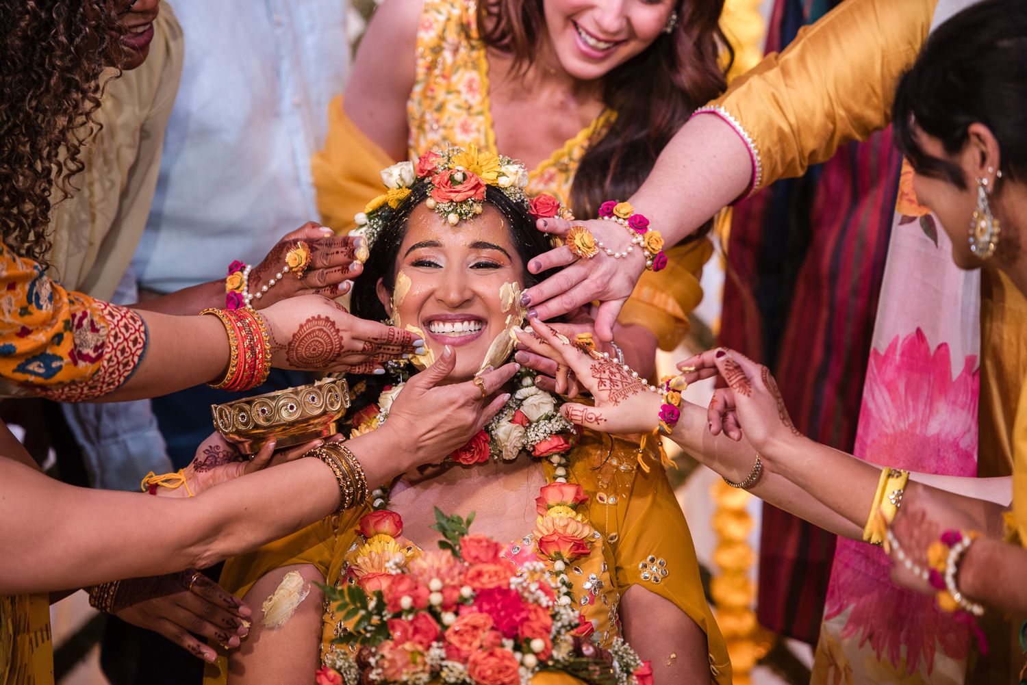 Joyful guests playfully feed turmeric and sweets during a traditional Haldi ceremony celebration.