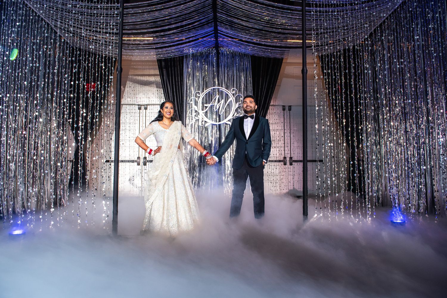 Dramatic wedding photo with fog effects and sparkly backdrop in purple-blue lighting.