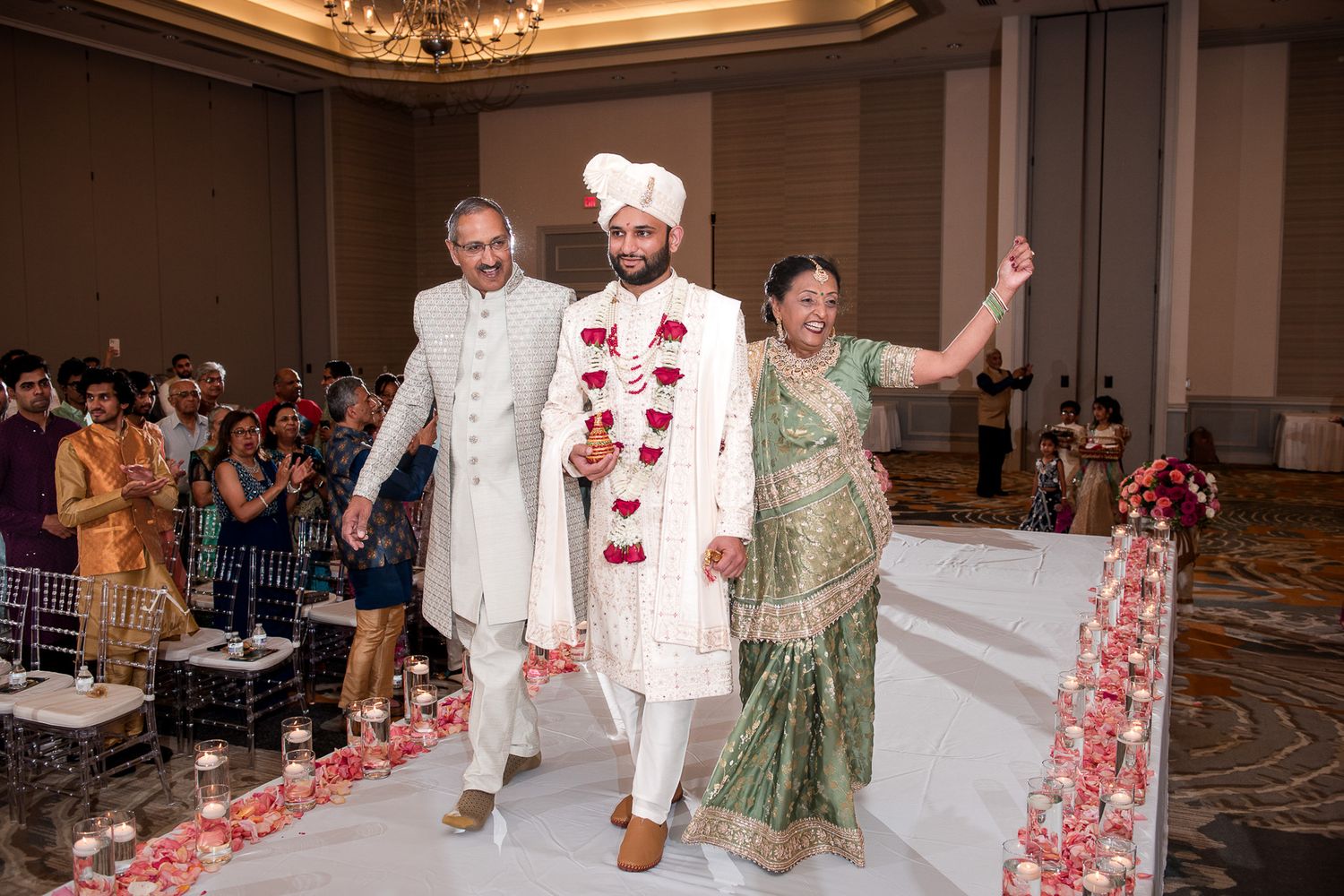Festive wedding ceremony processional walking down aisle in ballroom with flower petals.