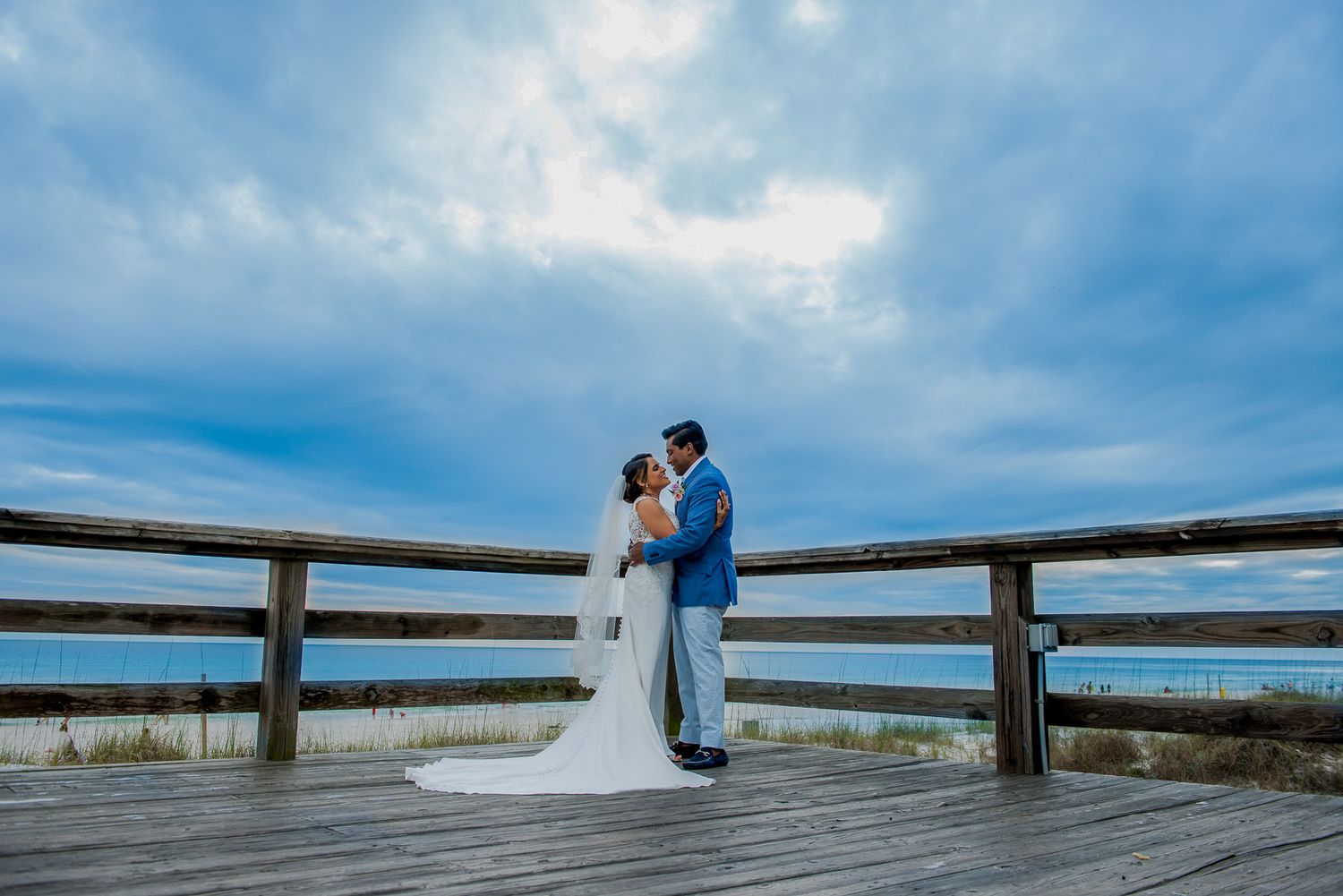 Romantic wedding portrait on wooden pier with dramatic cloudy sky backdrop.